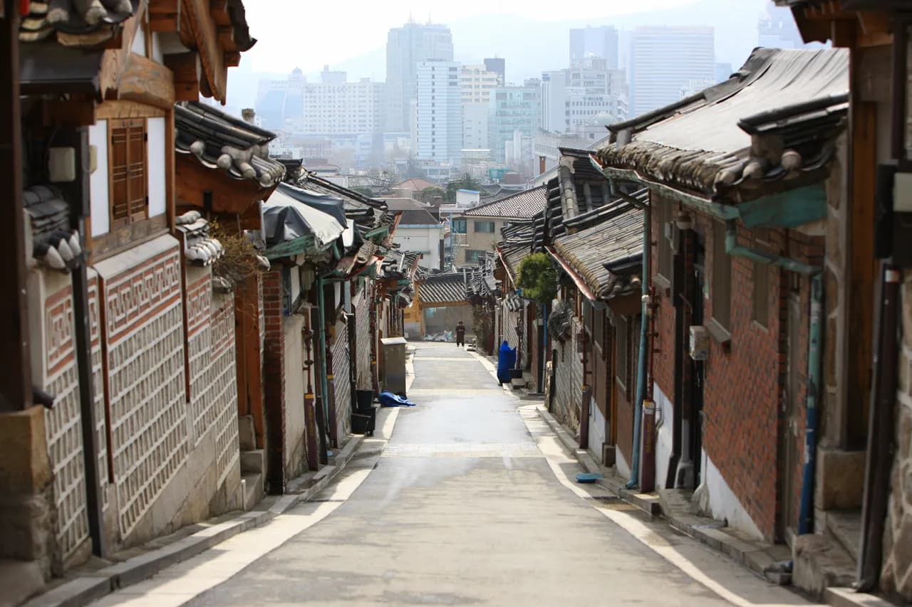 A traditional hanok alley in Bukchon descending toward the hazy summer Seoul skyline