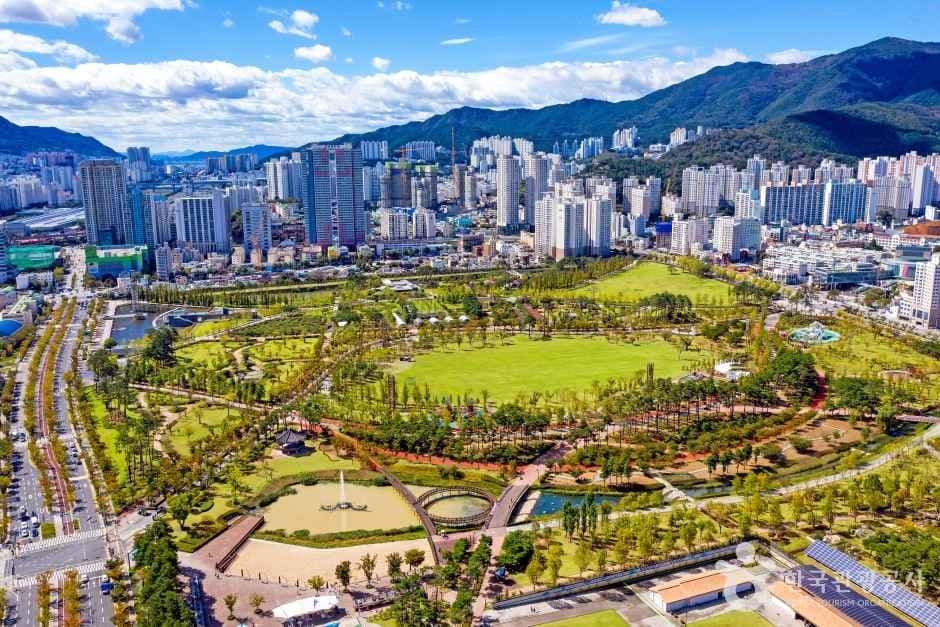 An aerial view of the large green Busan Citizens Park with the city and mountains behind