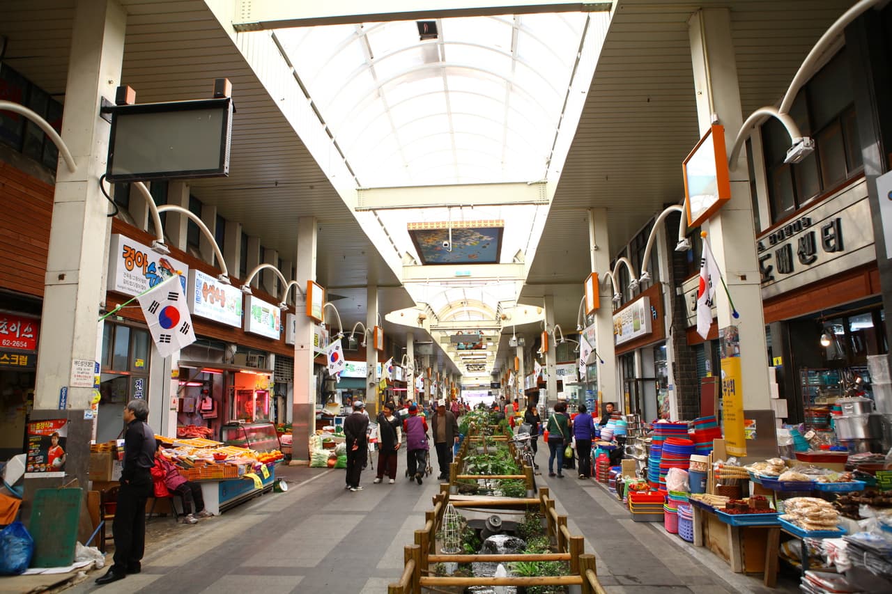 The covered aisle of Seogwipo Maeil Olle Market with shops and shoppers, Jeju