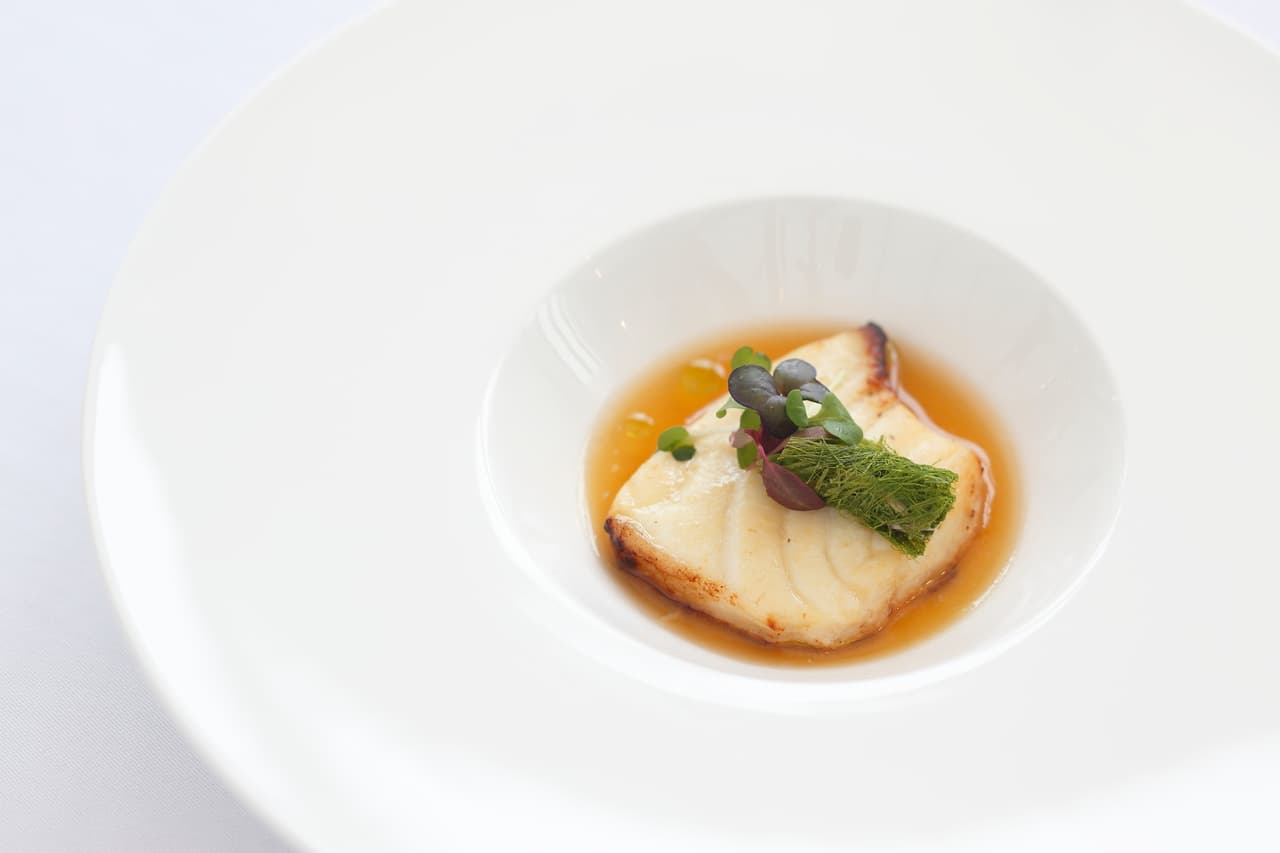 A delicate plated fish course in a light broth with microgreens at a fine-dining restaurant