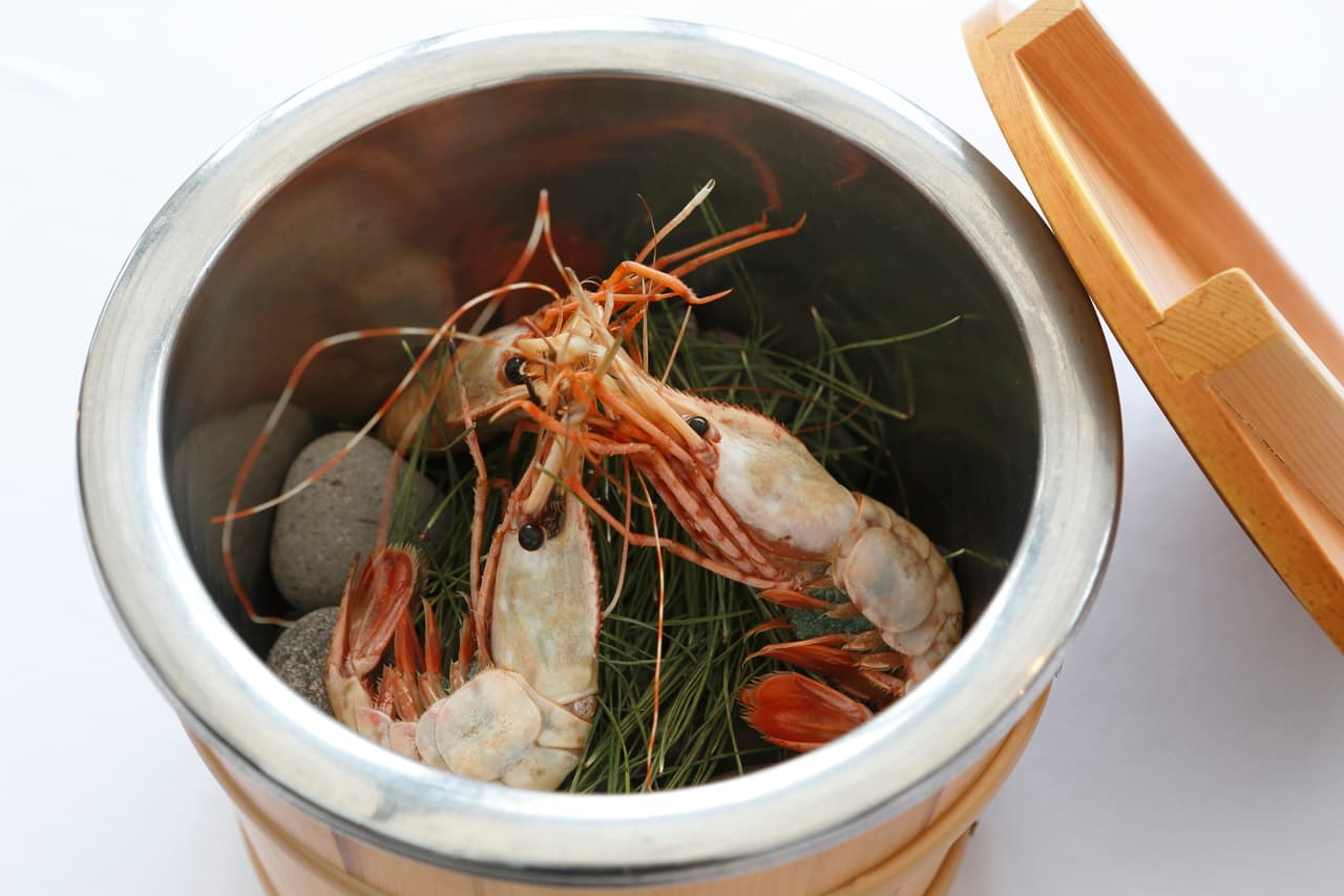 An artful presentation of prawns on herbs and stones in a metal vessel with a wooden lid