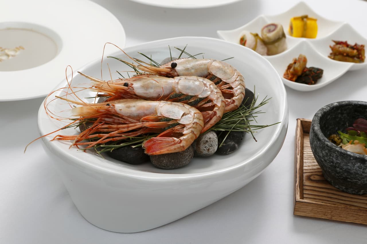 A plated Korean meal of grilled prawns with assorted side dishes on a white table