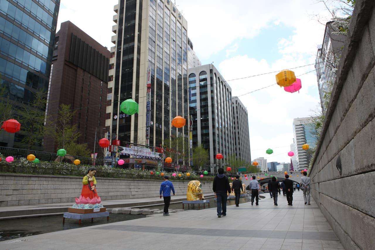 People strolling along the Cheonggyecheon stream past modern buildings in central Seoul