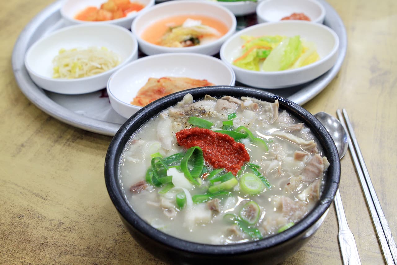 A bowl of dwaeji gukbap (pork-and-rice soup) with red spicy paste and side dishes