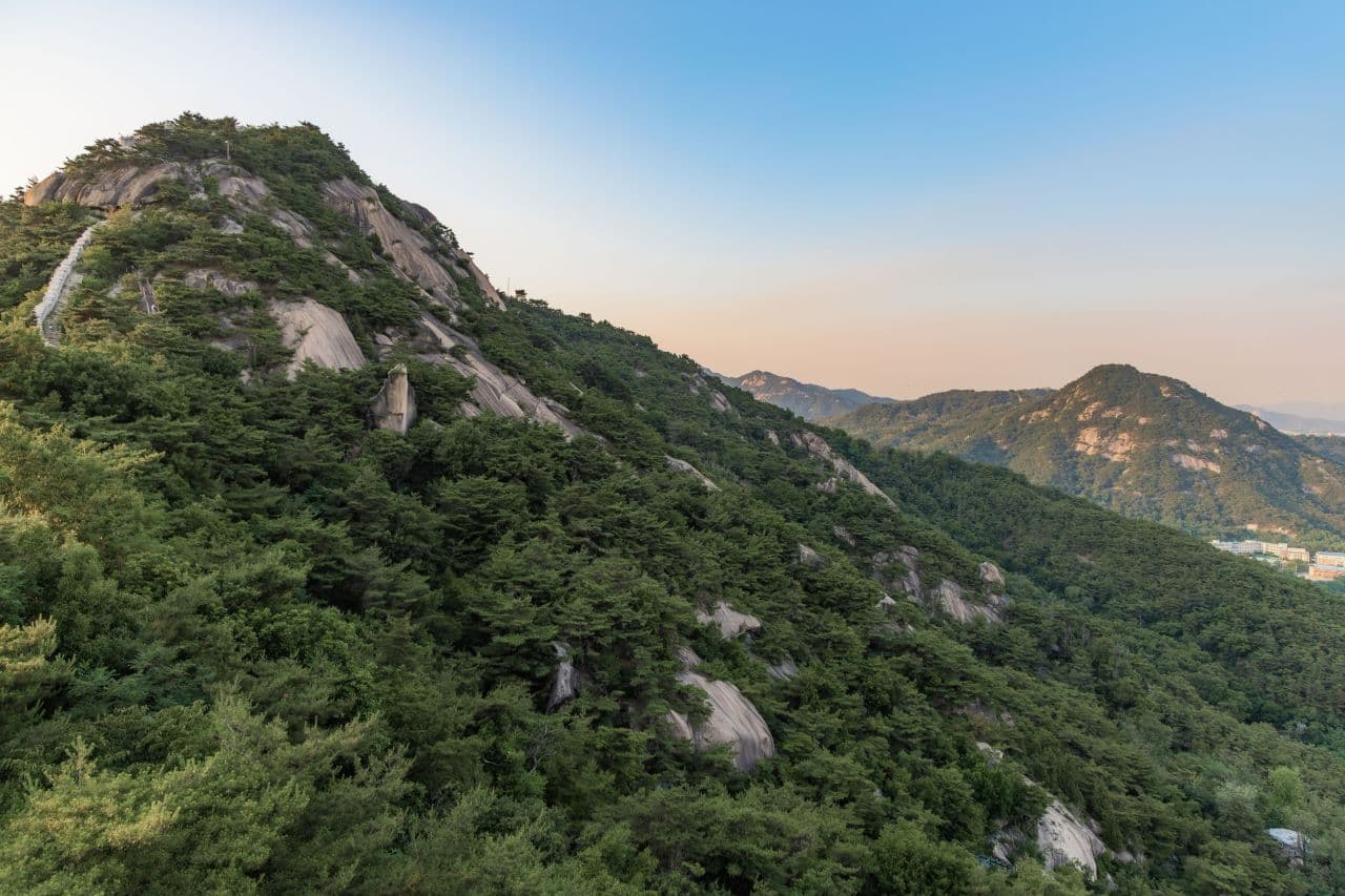 A forested granite ridge with a trail line, on a mountain near Seoul at dusk