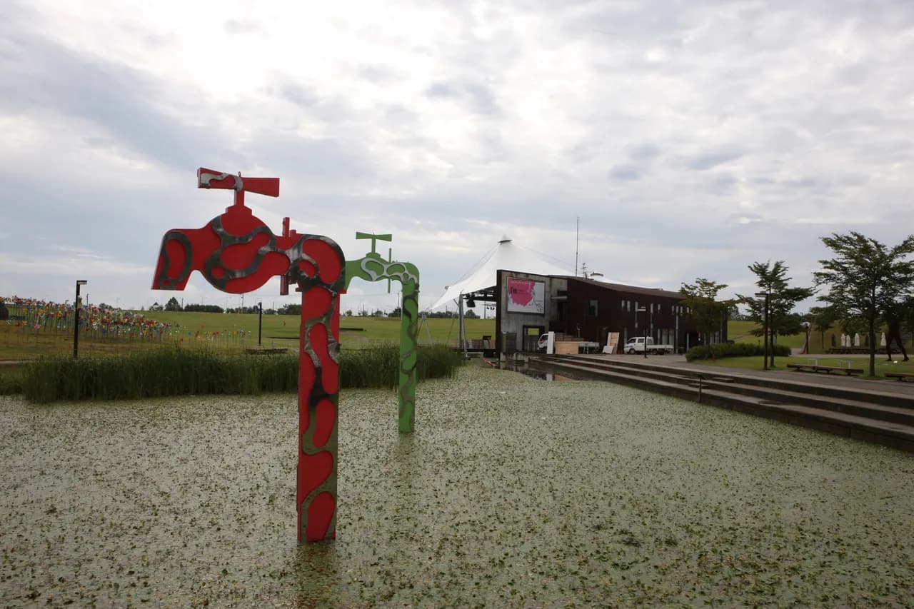 A wide peace-themed sculpture park with pinwheels and green lawns under a cloudy sky