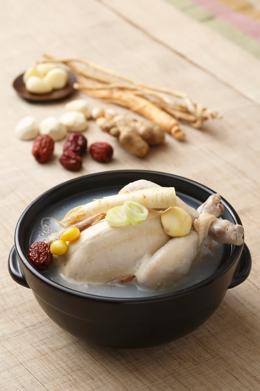 A bowl of samgyetang with ginseng root, jujube, and garlic on the table