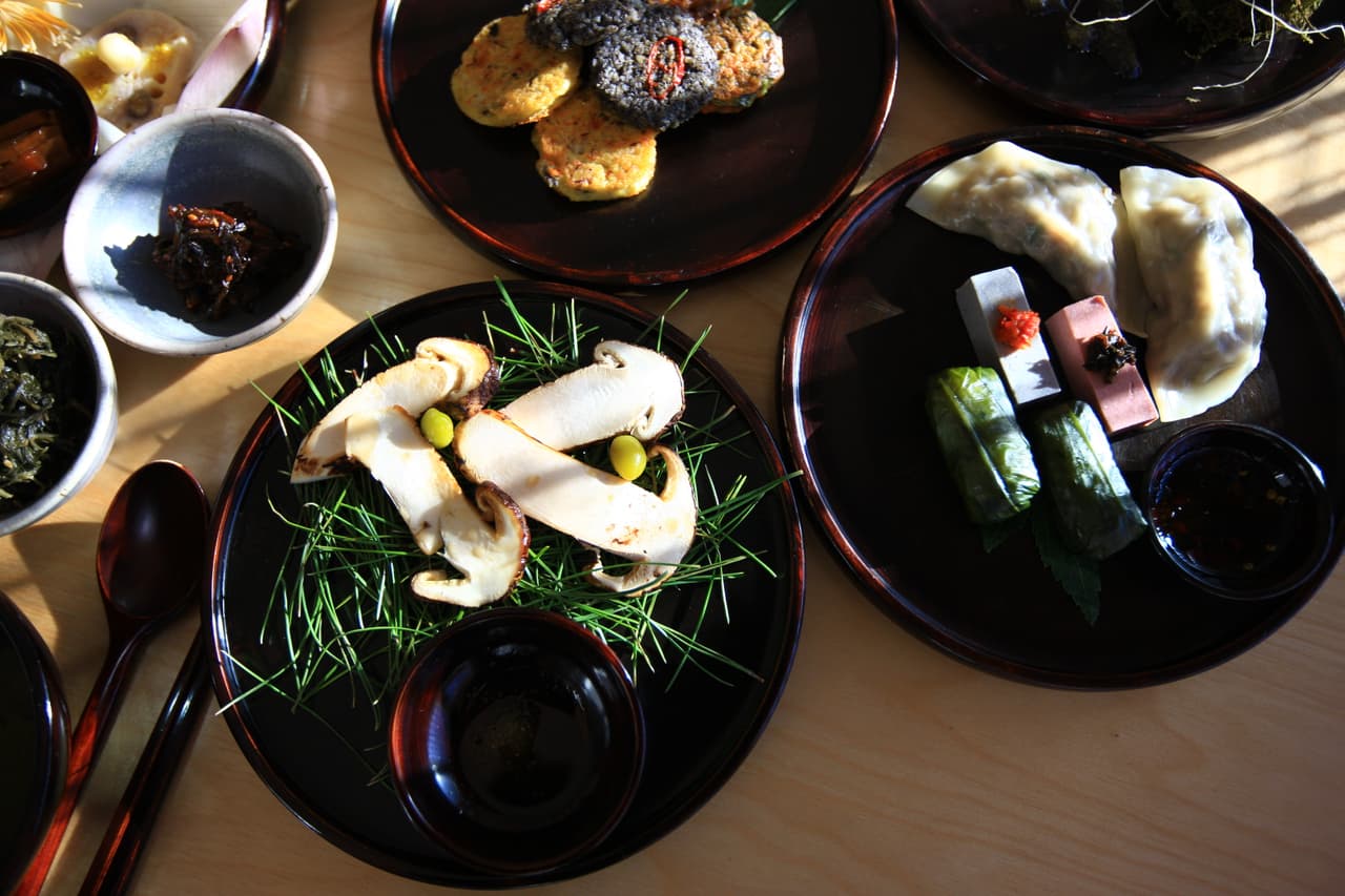 A spread of Korean temple cuisine — mushrooms, dumplings, and vegetable dishes on black lacquer plates