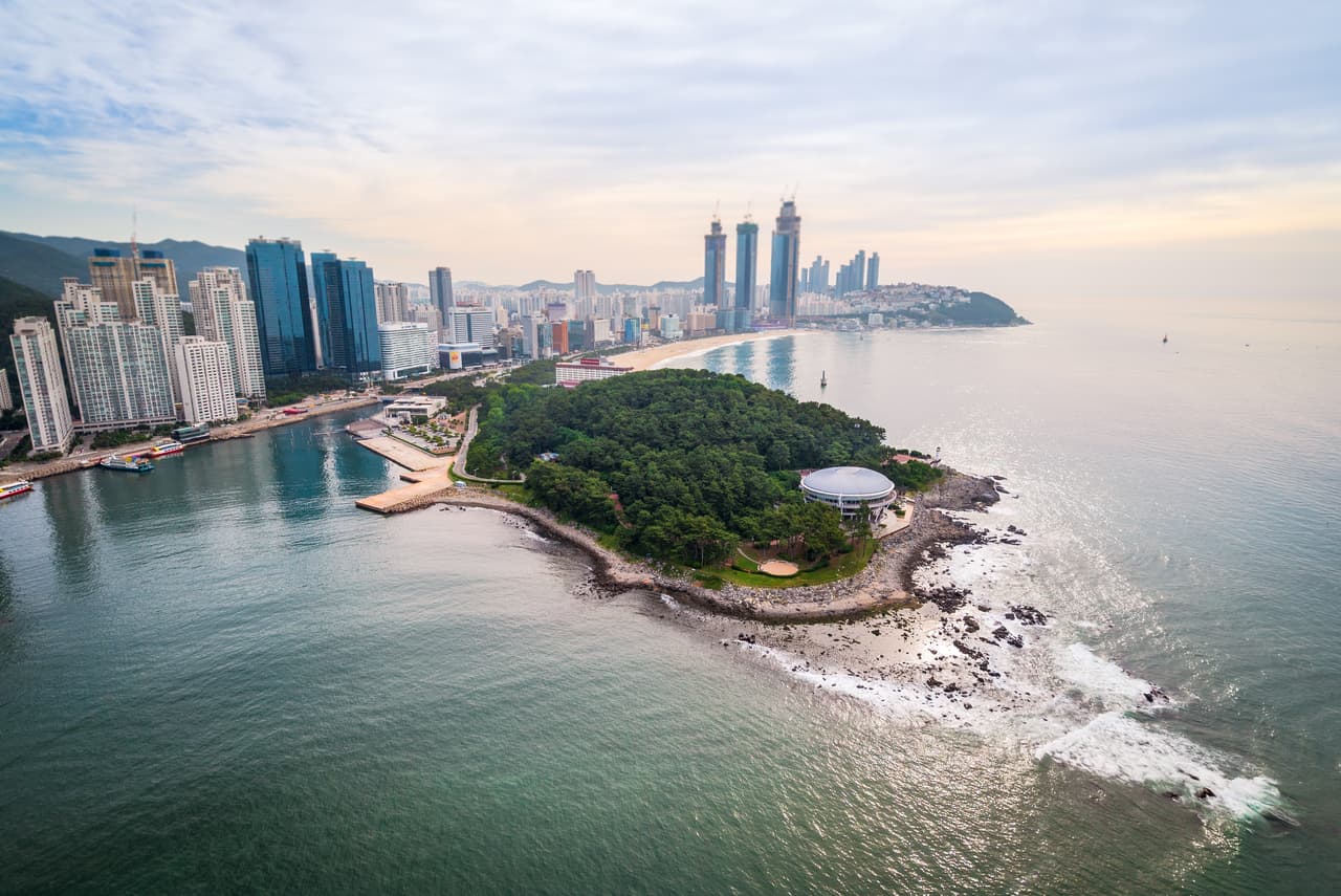 An aerial view of the wooded Dongbaekseom headland and the Marine City high-rises in Haeundae, Busan