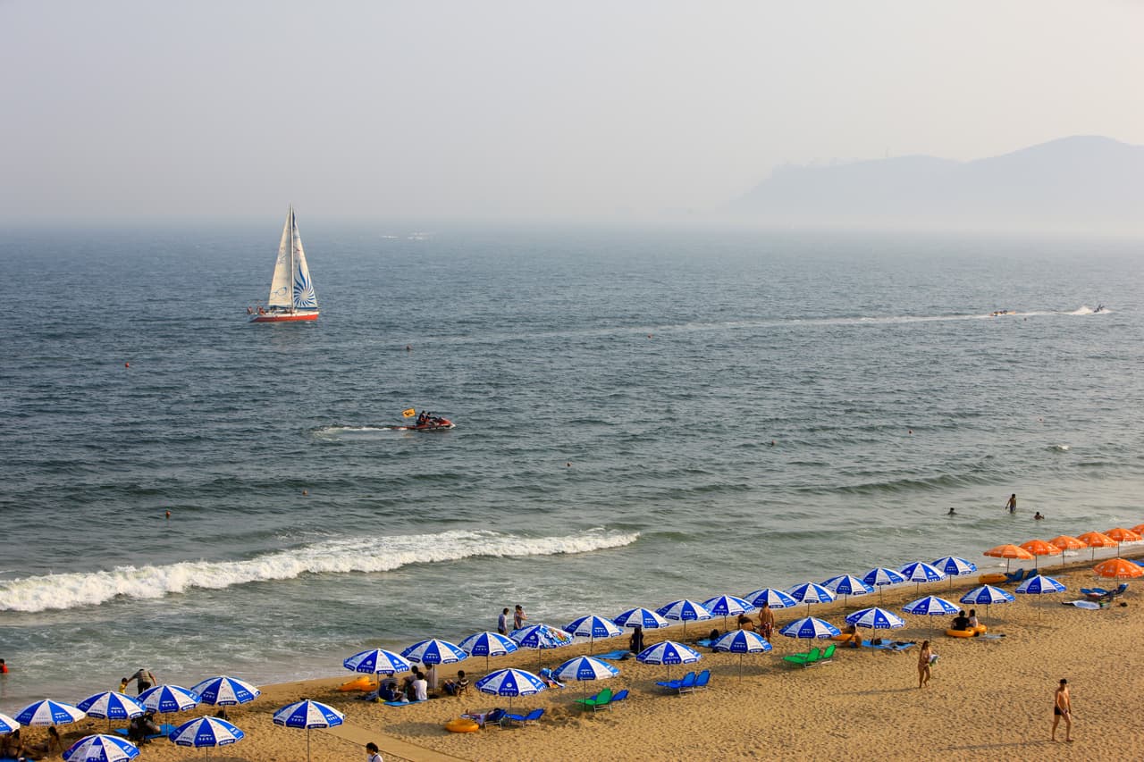 Haeundae Beach in Busan during the day, with parasols and a sailboat offshore