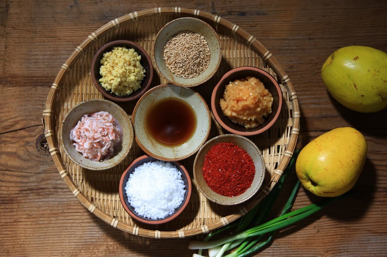 Small bowls of kimchi-making ingredients including chili powder, garlic, fish sauce, and salted shrimp
