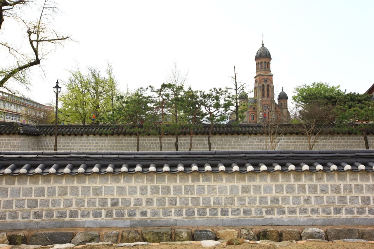 The tiled stone wall of Gyeonggijeon Shrine with Jeondong Catholic Cathedral behind it
