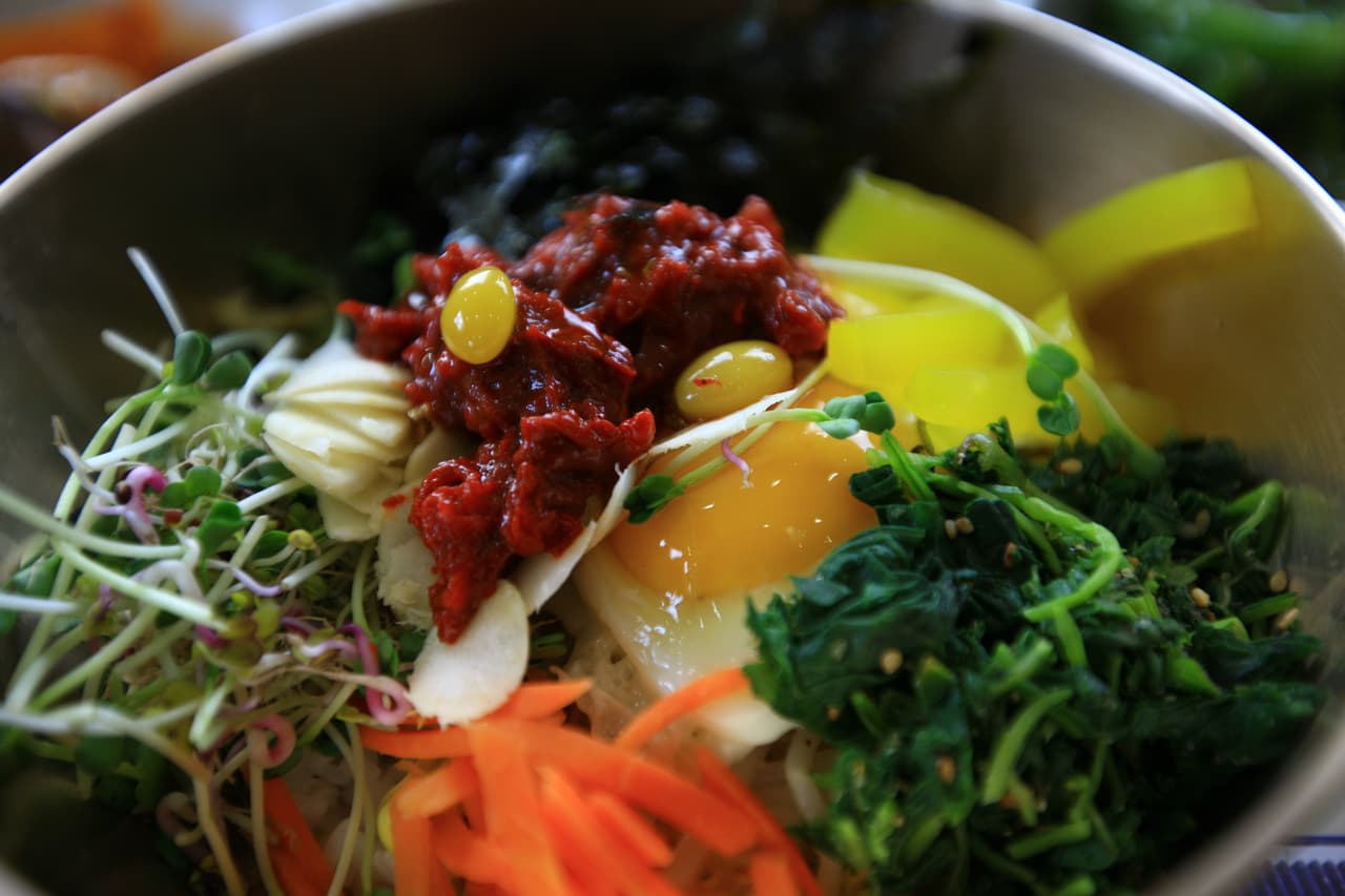 A bowl of Jeonju bibimbap topped with seasoned vegetables, egg yolk, and beef