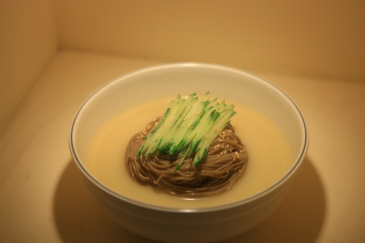 A bowl of makguksu — cold buckwheat noodles topped with cucumber in a light broth