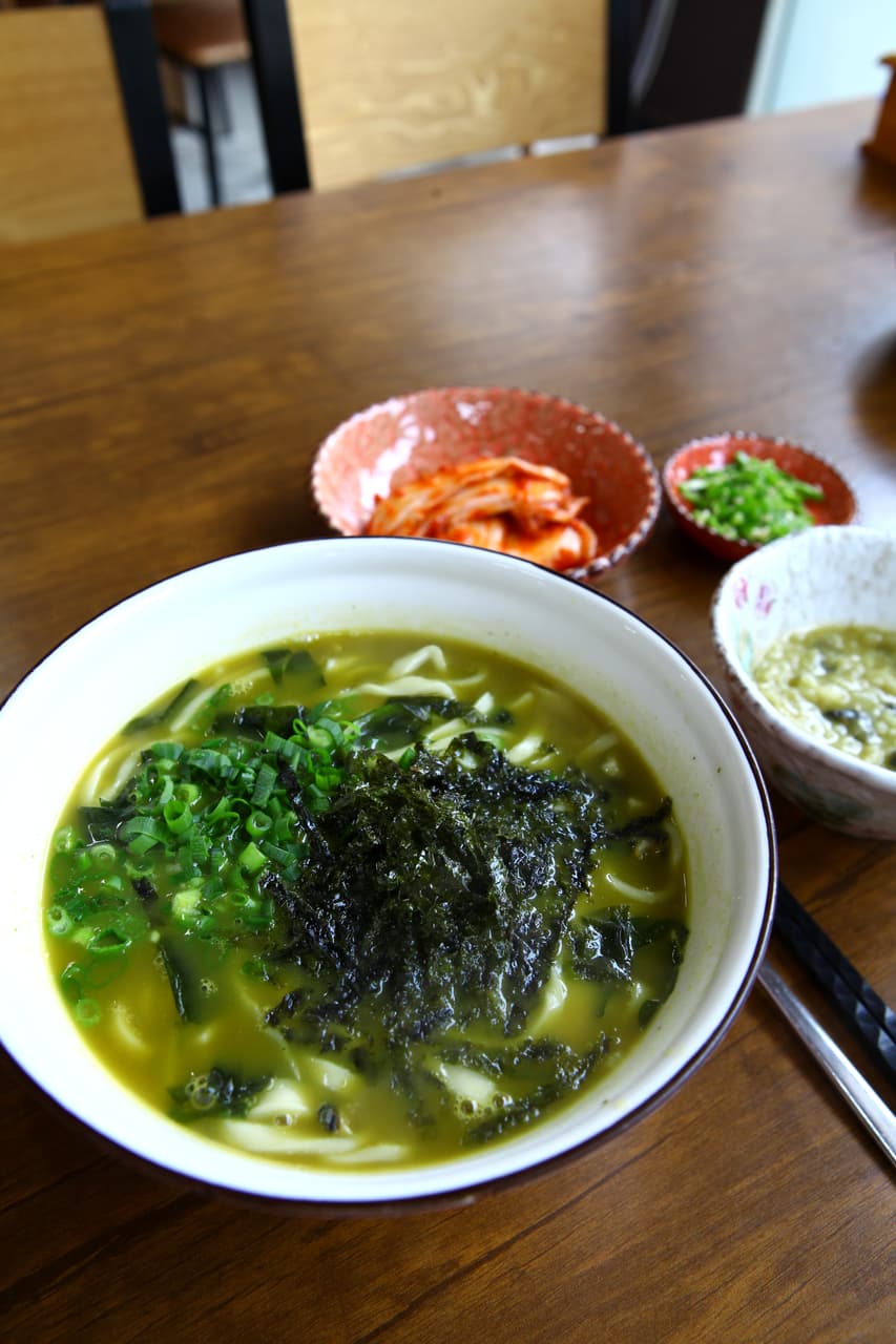 A bowl of kalguksu — knife-cut noodles in broth with seaweed and scallion — with kimchi on the side