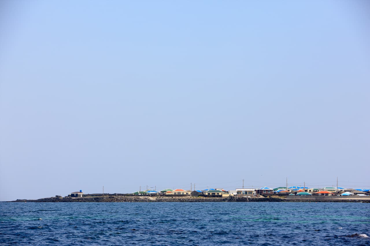 A calm blue sea with a low island village of colorful rooftops on the horizon
