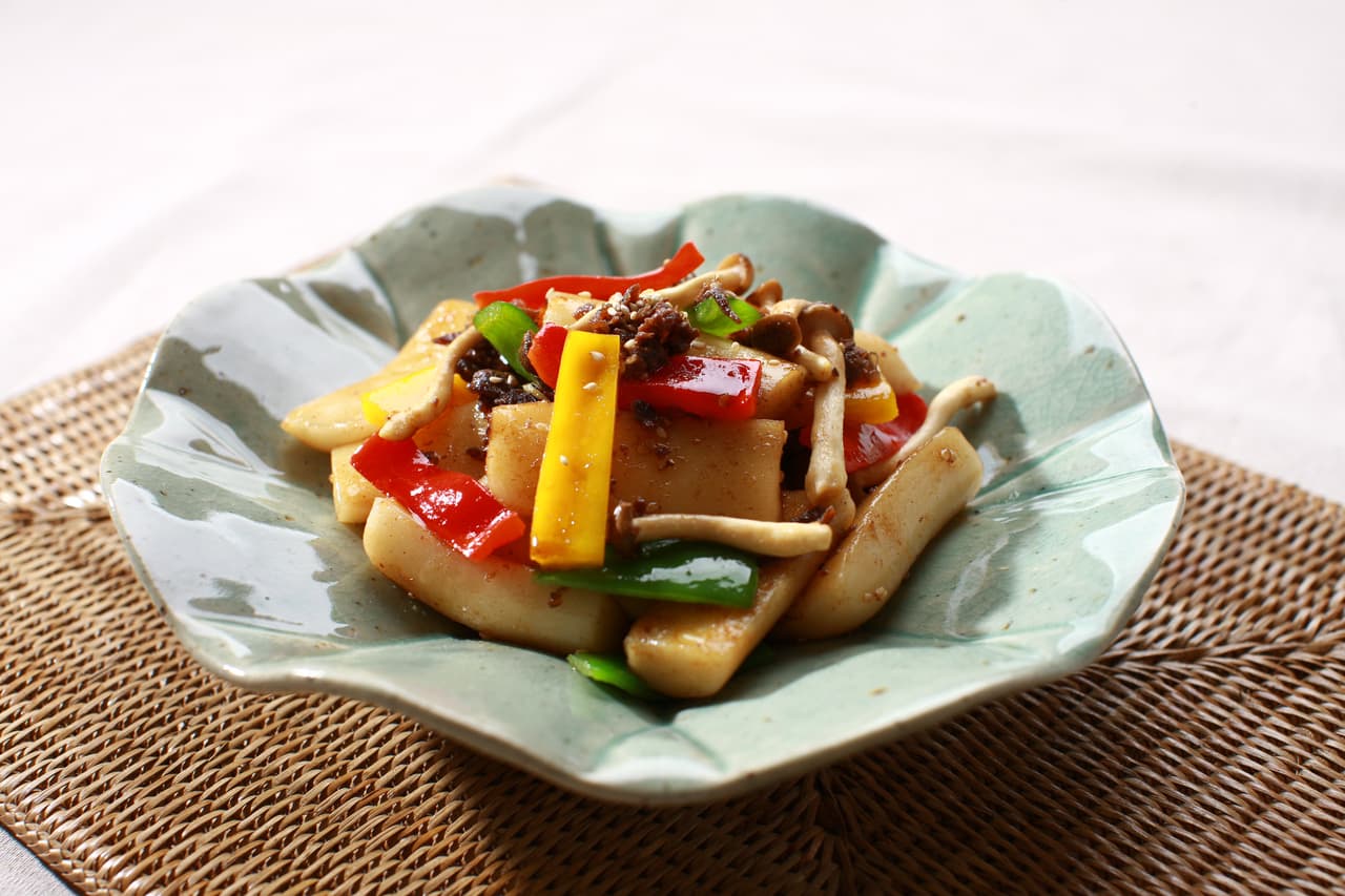 A plate of soy-sauce tteokbokki with rice cakes, peppers, and mushrooms