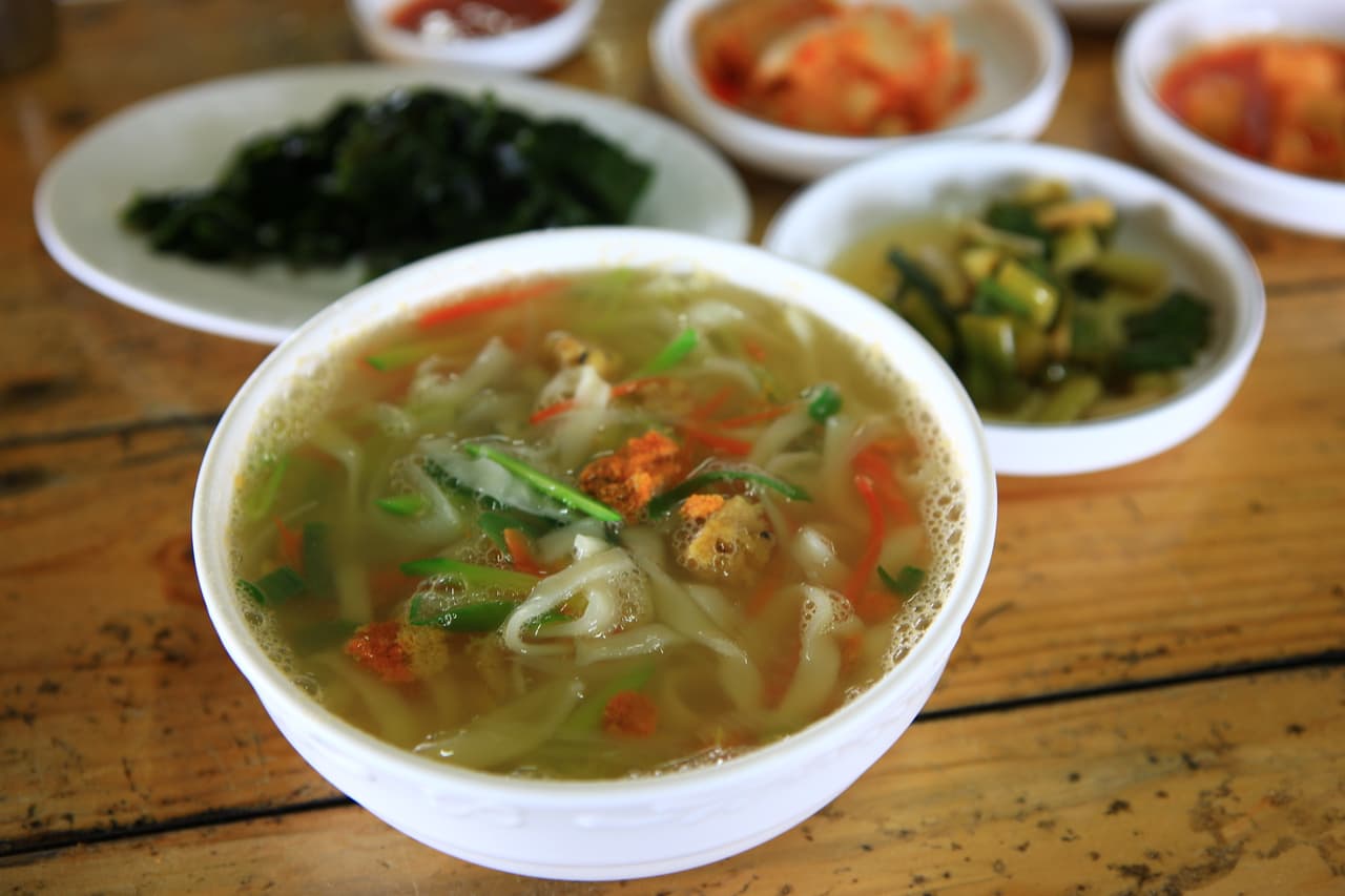 A bowl of Korean kalguksu (knife-cut noodle soup) with vegetables and side dishes