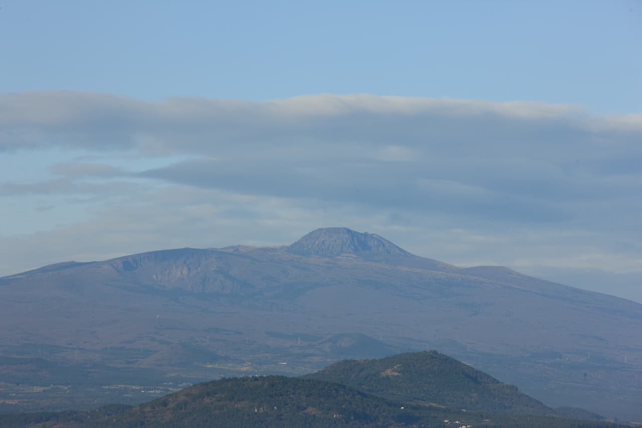 Hallasan volcano seen from a distance, with forested oreum cones in the foreground
