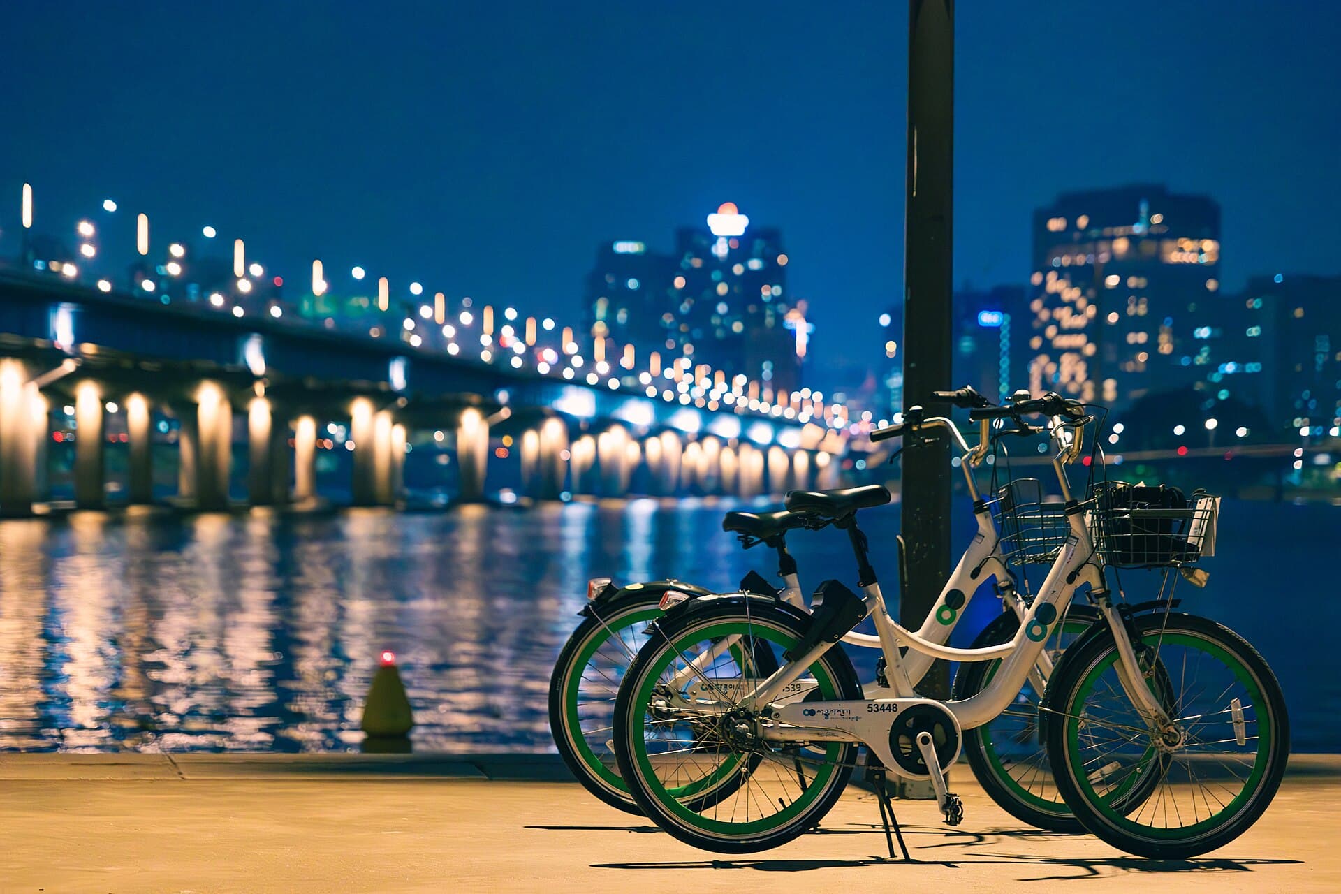 Rental bicycles parked along the Han River with a lit bridge in the background at night