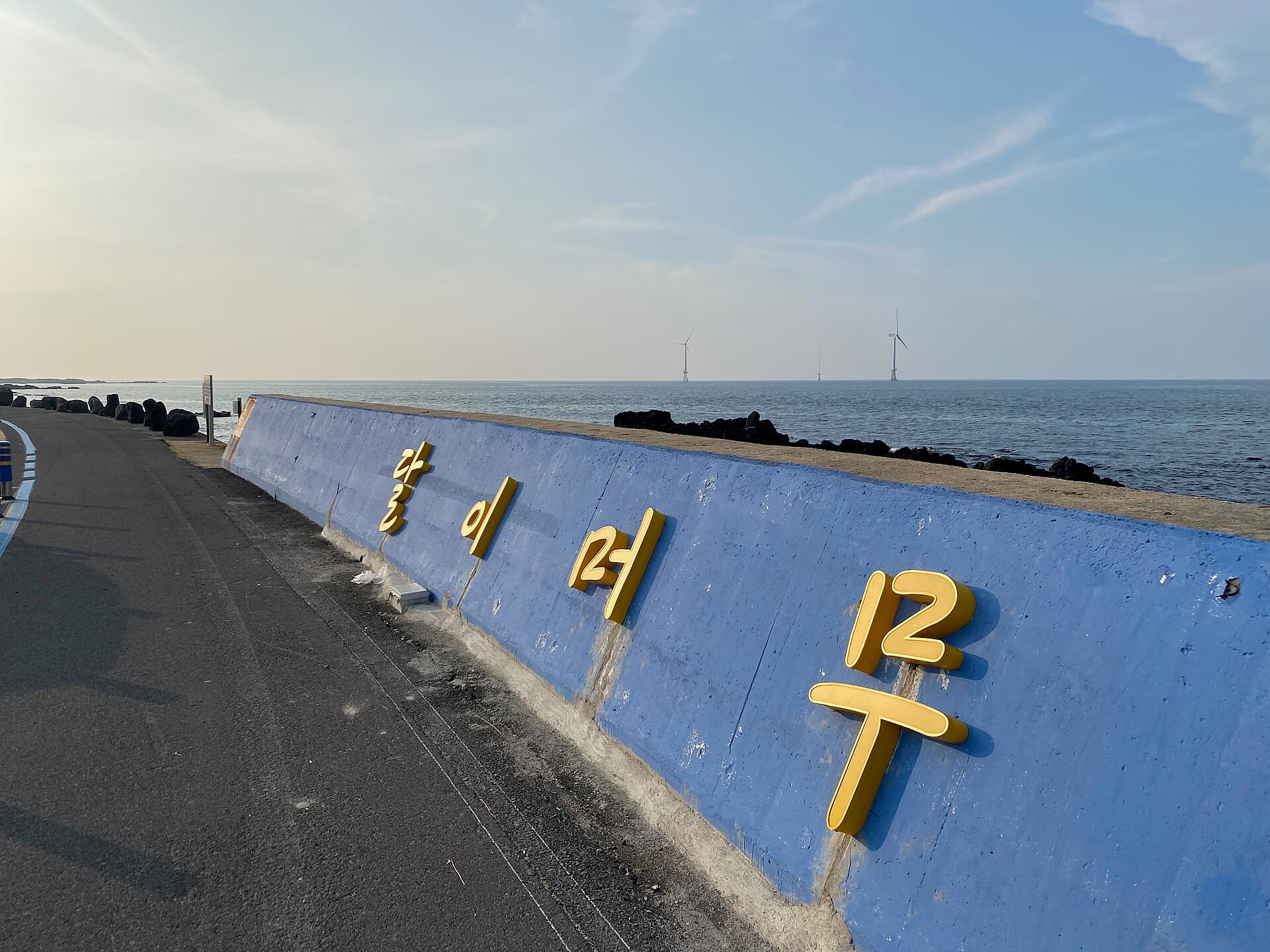Offshore wind turbines seen from Woljeongri Beach's painted sea wall on Jeju