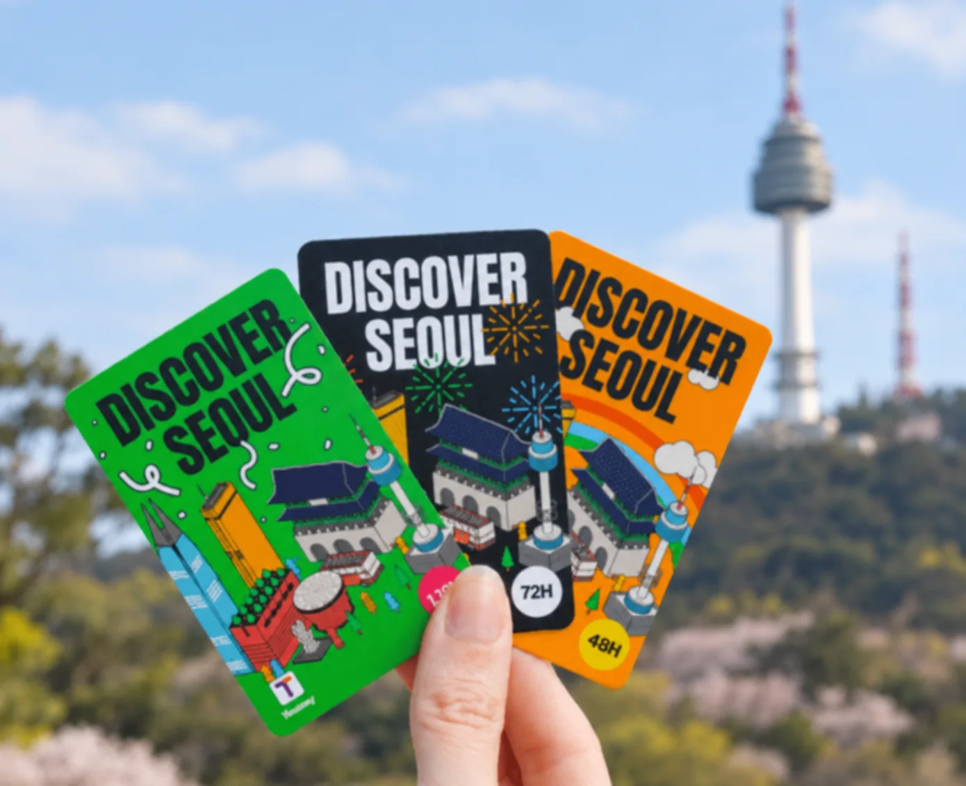 Three Discover Seoul Pass cards in green, black and orange held up in front of N Seoul Tower