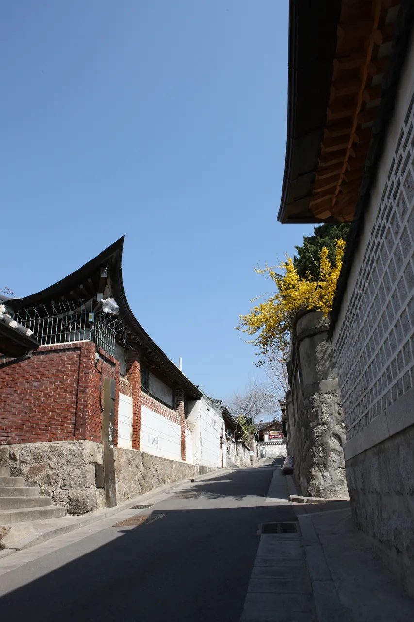 A quiet sloping lane of traditional tiled-roof hanok houses under a clear blue sky