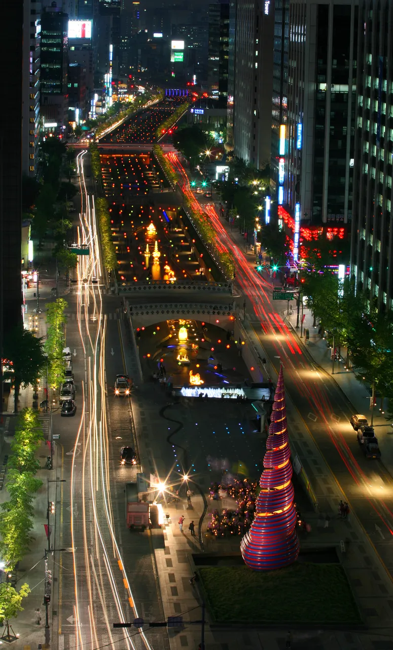 An aerial night view of a lit stream corridor running between city towers with light trails