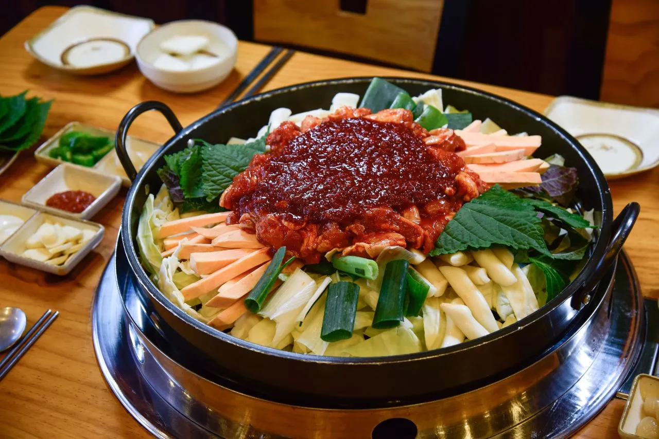 A large iron pan of dakgalbi: spicy marinated chicken with cabbage, rice cakes, and vegetables