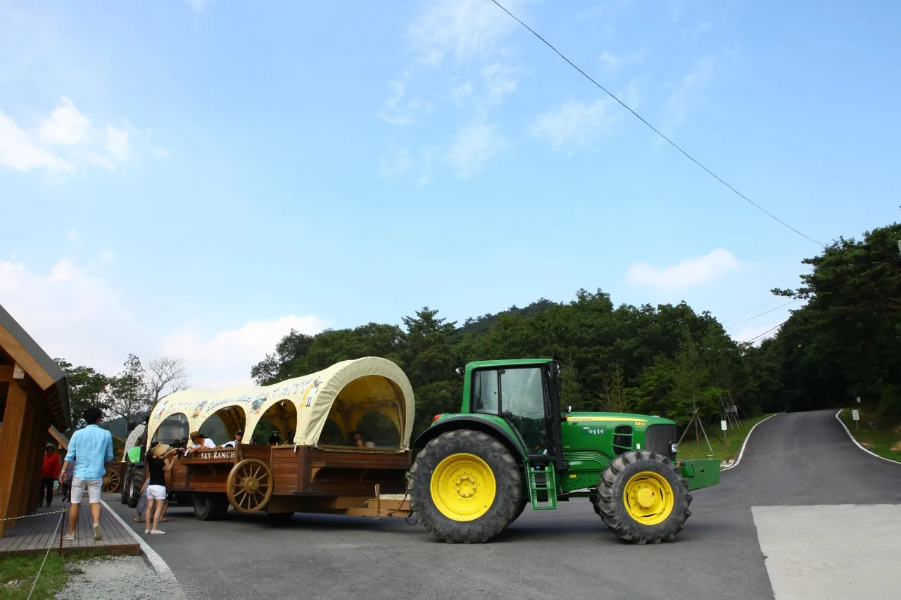 A tractor pulling a multi-row carriage across green pasture at Daegwallyeong Sky Ranch