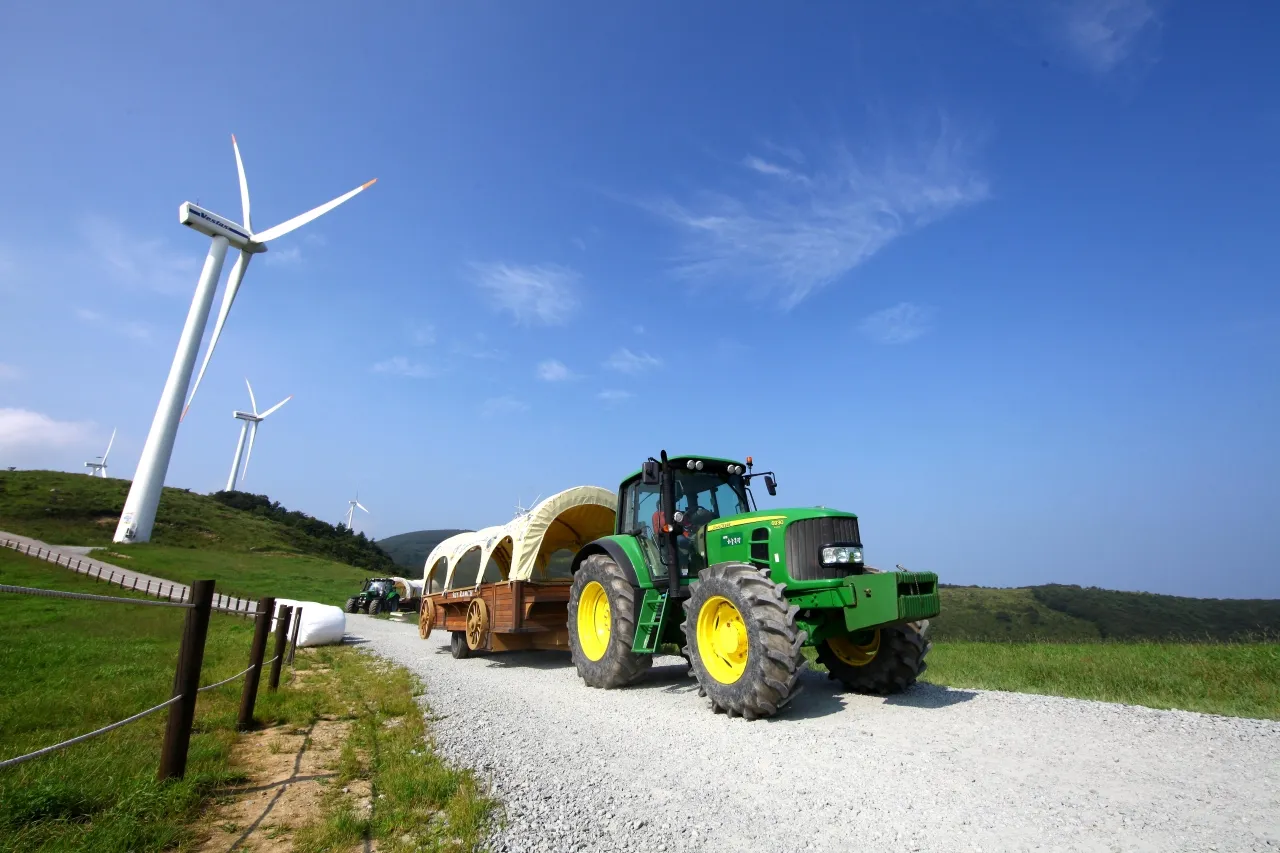 Tractor carriages on a dirt ranch road at Daegwallyeong Sky Ranch with wind turbines on distant hills
