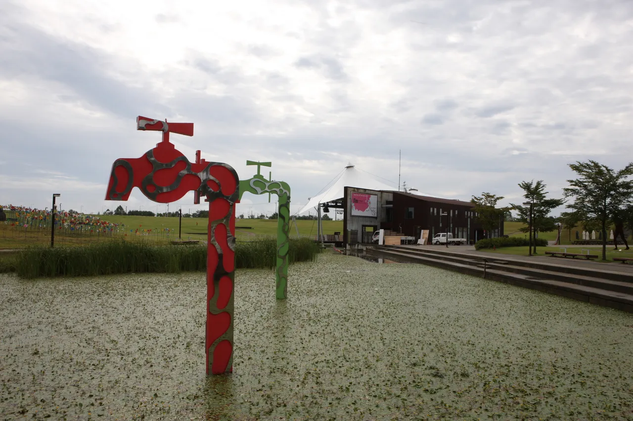 A wide peace-themed sculpture park with pinwheels and green lawns under a cloudy sky