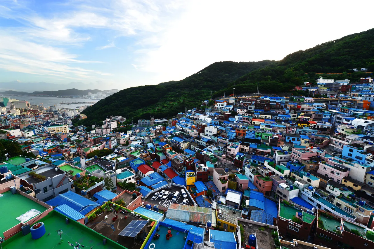 Terraced hillside houses in blue, red and green stacked up a slope above Busan's harbor