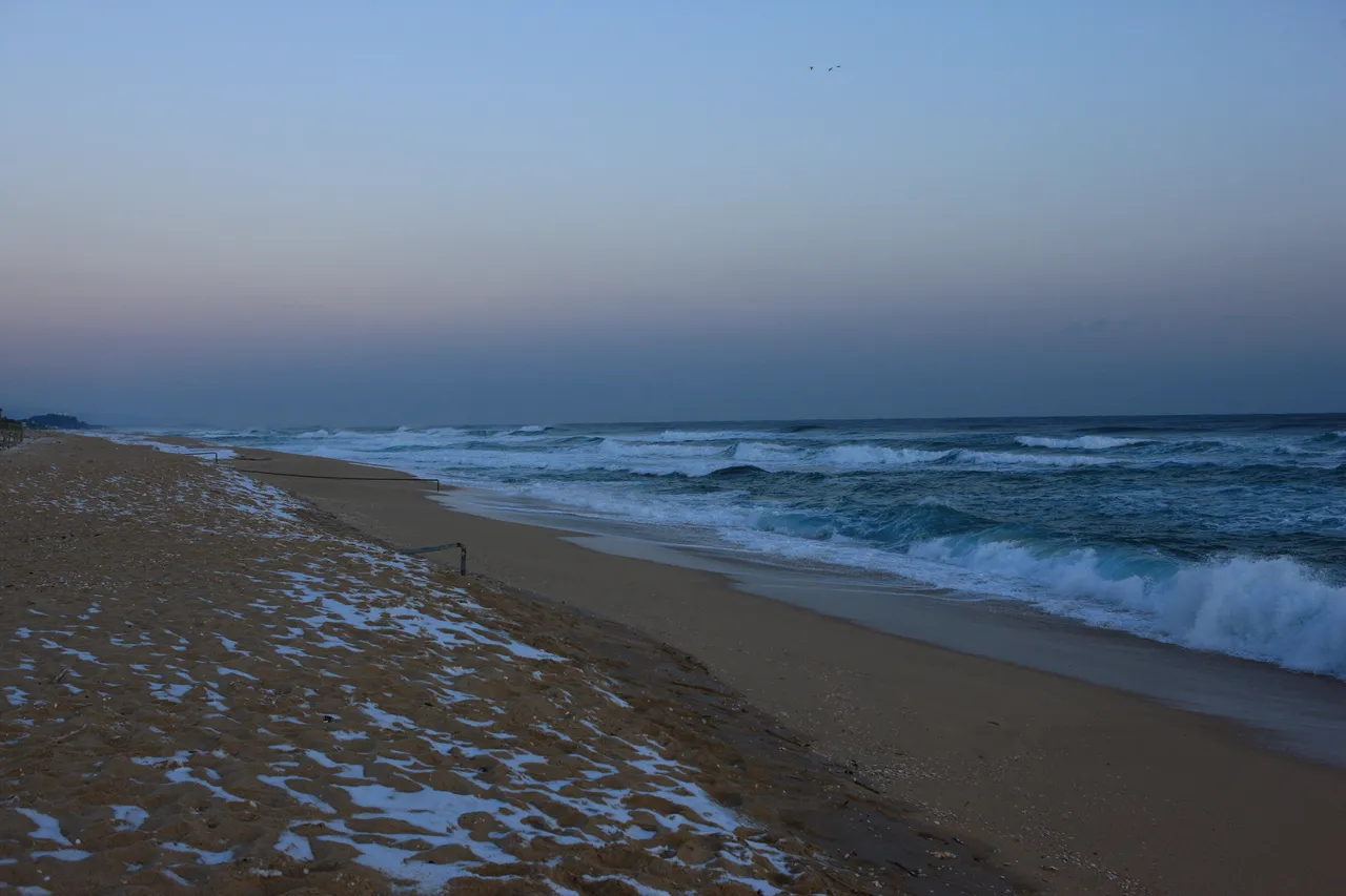 Waves on Anmok Beach in Gangneung at dawn, with patches of snow on the sand