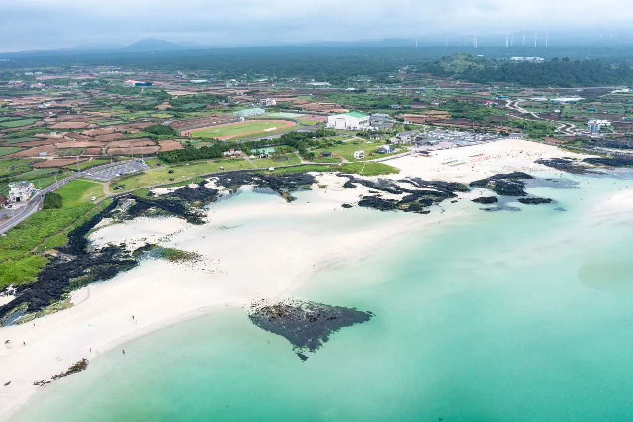 Aerial view of a curved white sandbar and turquoise water meeting dark lava rock along the shore