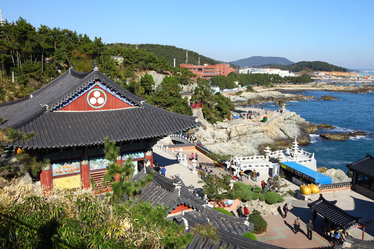 Tiled temple roofs on a hillside above a rocky coast, with the sea and a far headland in the distance