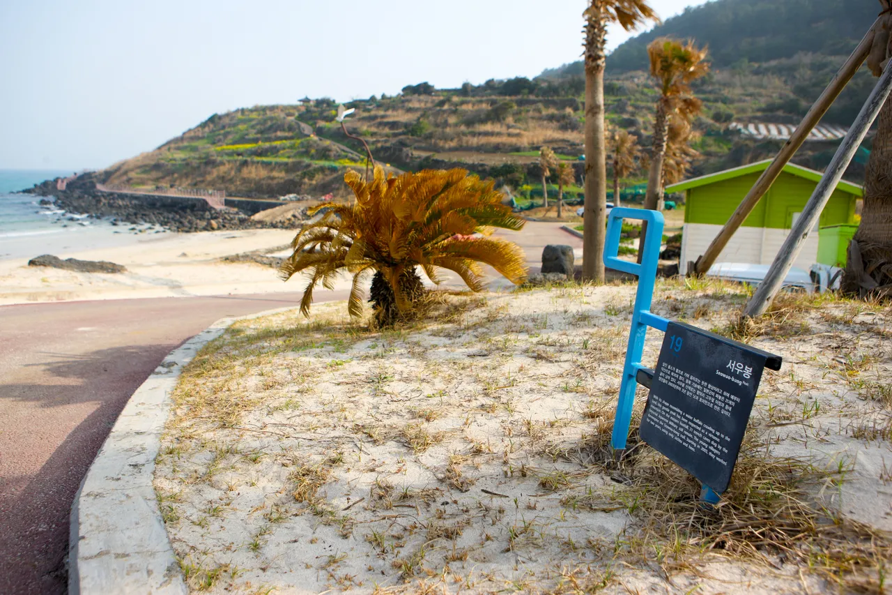 A sign for Seoubong beside the beach path, with a terraced green hillside behind