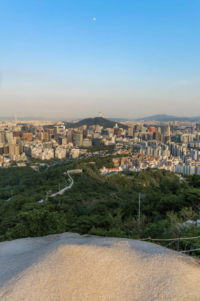 The Seoul skyline and an old city wall seen from a rocky mountain summit at dusk