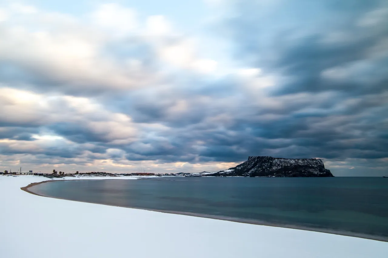 Snow on the shore with Seongsan Ilchulbong rising behind under low cloud