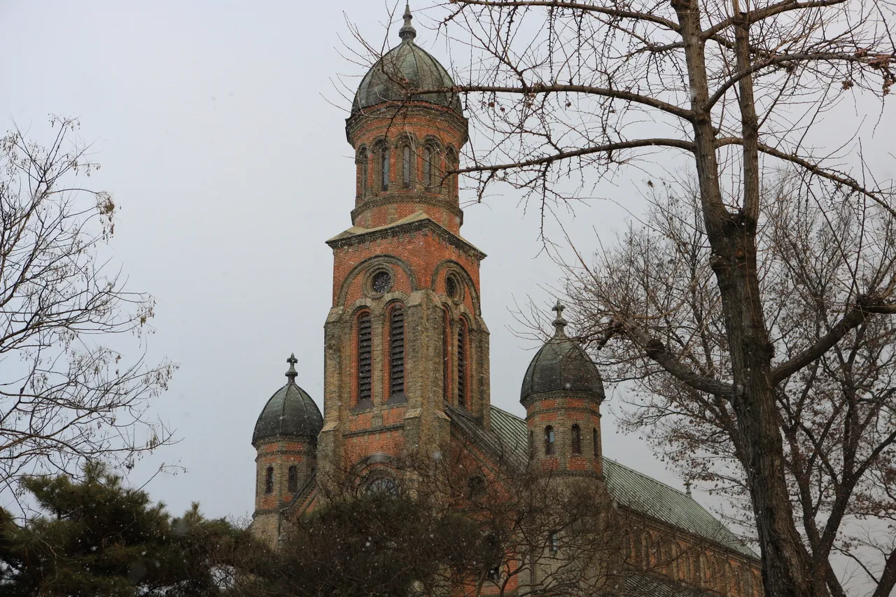 The brick bell tower of Jeondong Catholic Cathedral in Jeonju behind bare tree branches