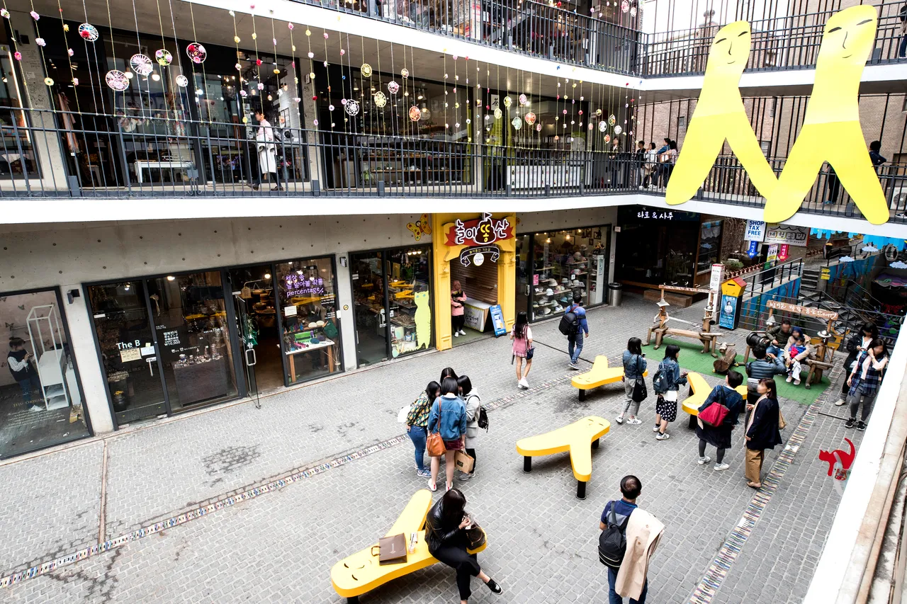 A busy pedestrian courtyard lined with small shops in a traditional Seoul arts district