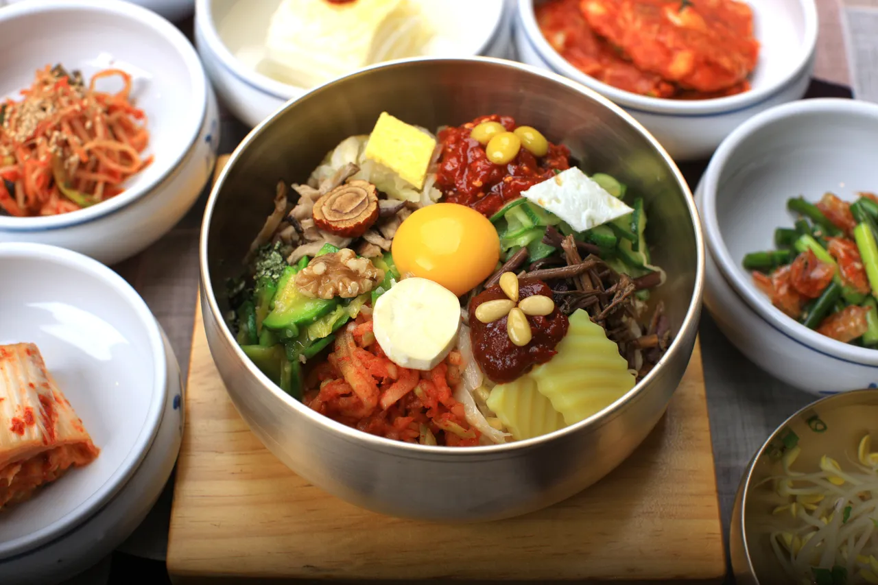 A bowl of Korean bibimbap with egg and vegetables, surrounded by small dishes of banchan