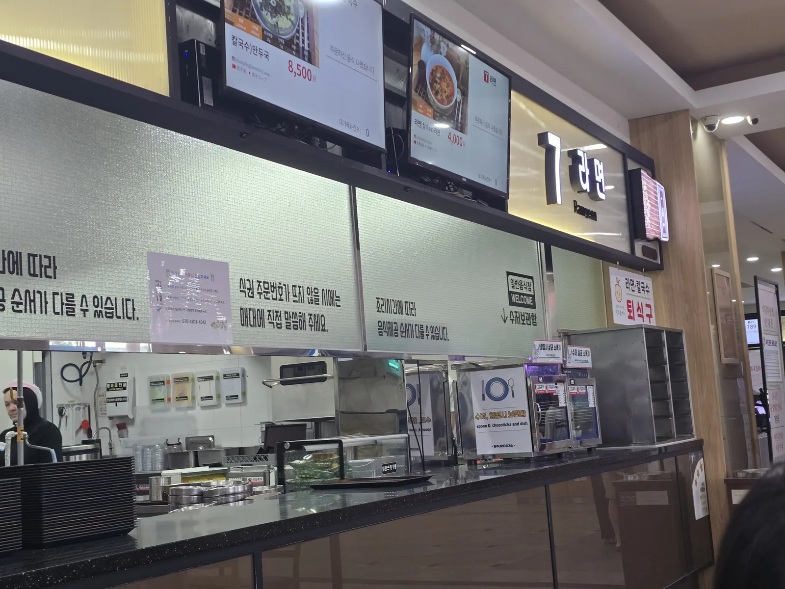 Two printed notices above a food court counter about ticket numbers and serving order