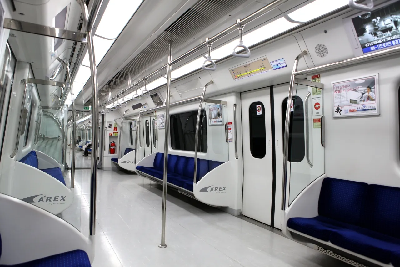The clean, empty interior of a modern airport-express train with blue seats and handrails