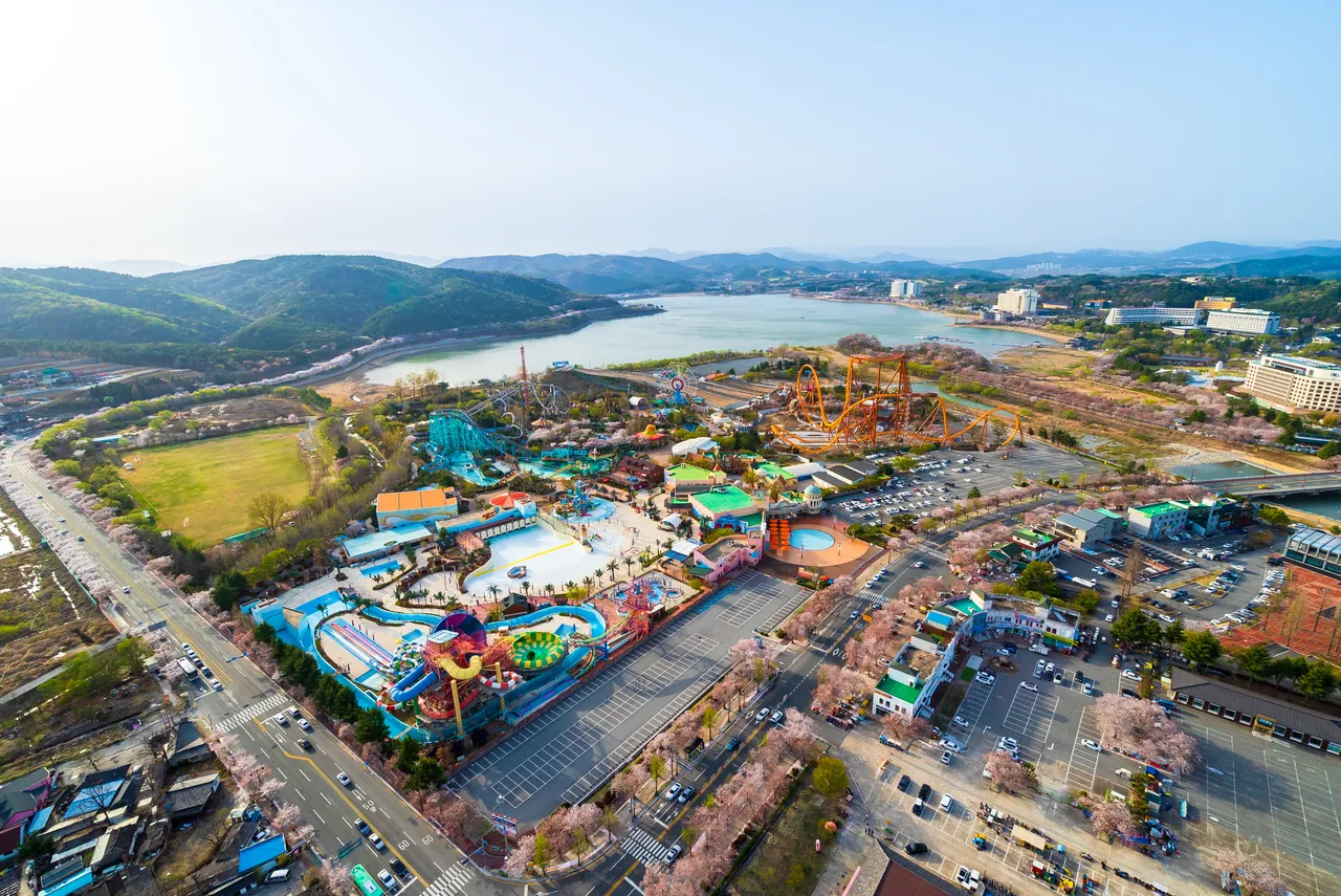 An aerial view of an amusement park with roller coasters beside a lake and green hills