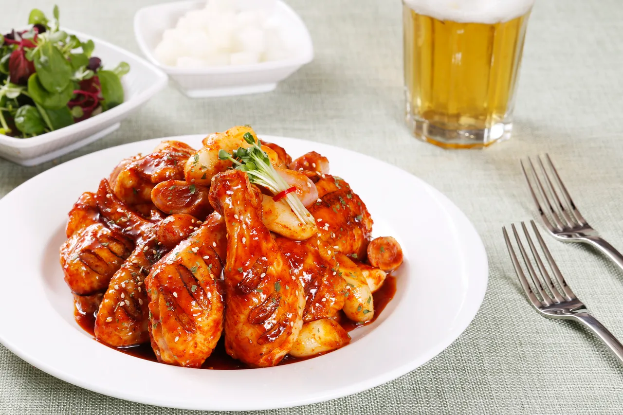 A plate of Korean sauced fried chicken with pickled radish and a glass of beer