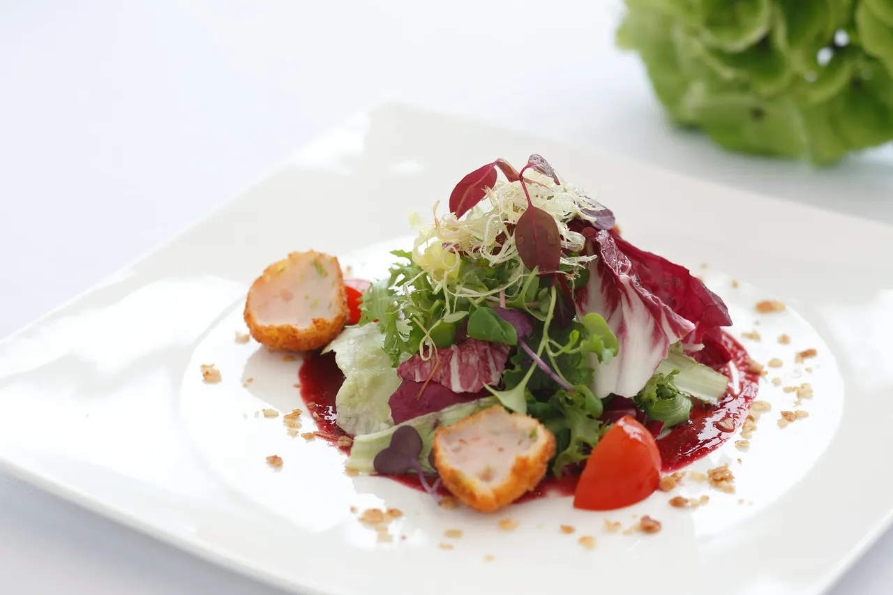 A refined plated fine-dining salad with microgreens and a fruit coulis on a white plate