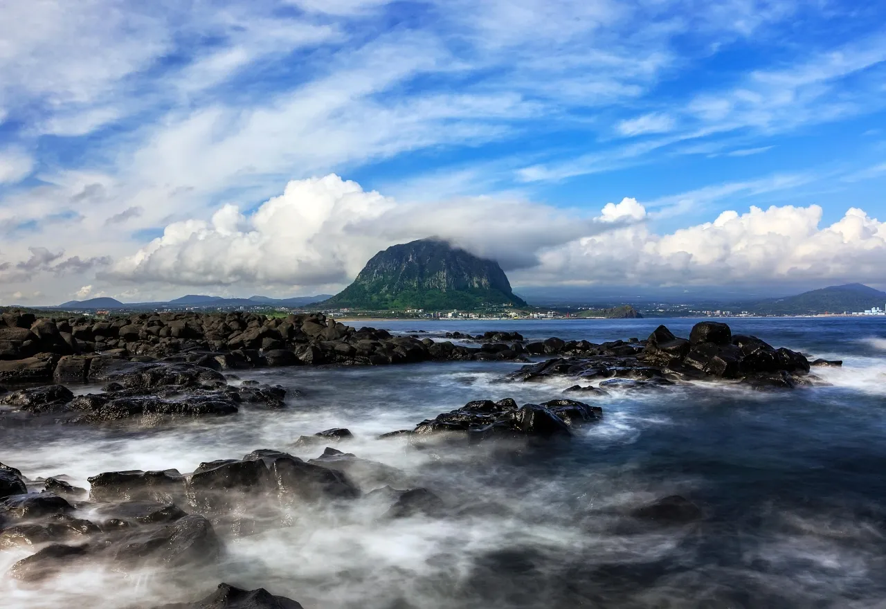 Sanbangsan mountain rising over the volcanic rock coast and sea of Jeju Island