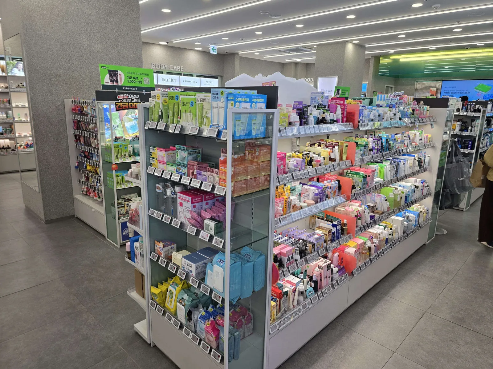 A deep skincare aisle inside a large Olive Young store with a body-care section beyond