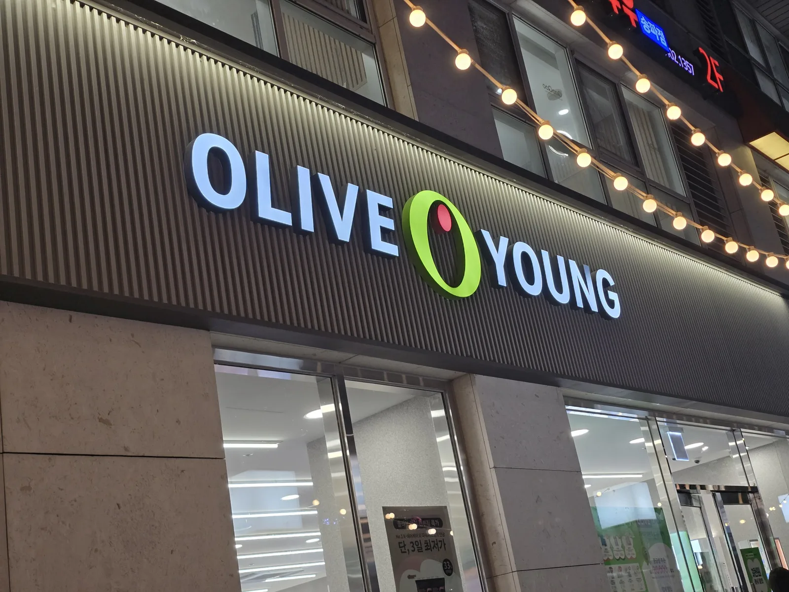 The lit Olive Young storefront sign above a store entrance at night